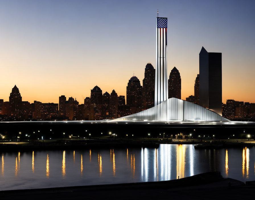 City skyline at dusk with tall building and American flag amidst illuminated buildings and calm water reflections