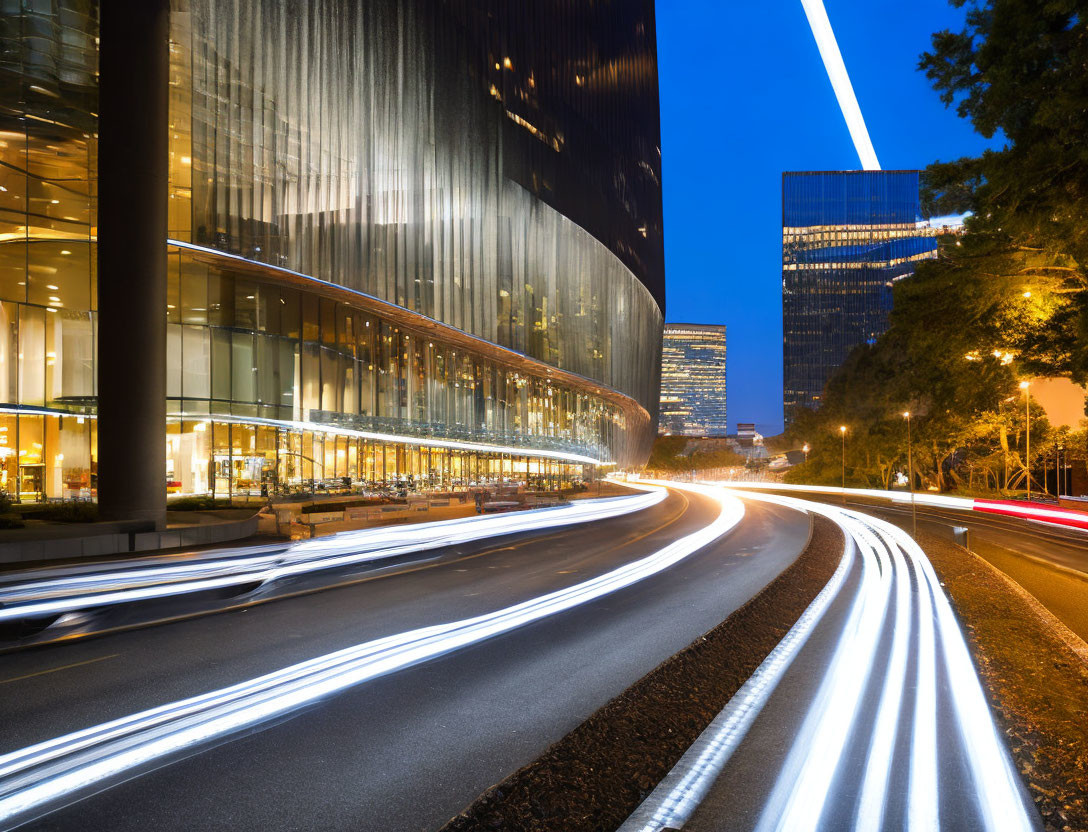 Urban night scene with car light streaks and modern buildings.