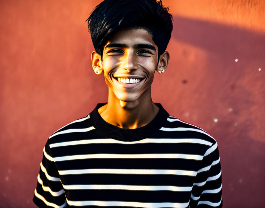 Smiling young man in striped shirt against orange wall in golden sunlight