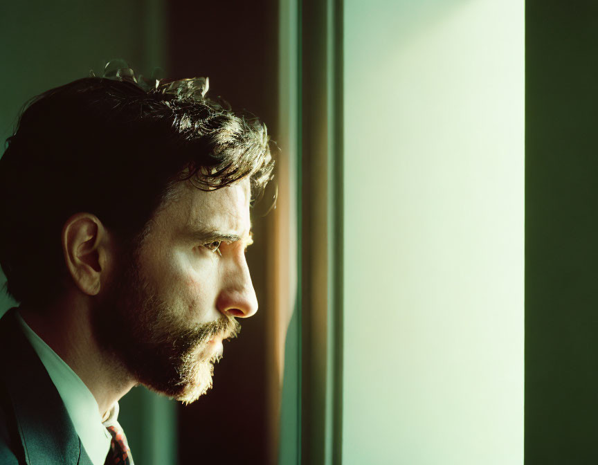 Man in suit gazes out window in warm sunlight