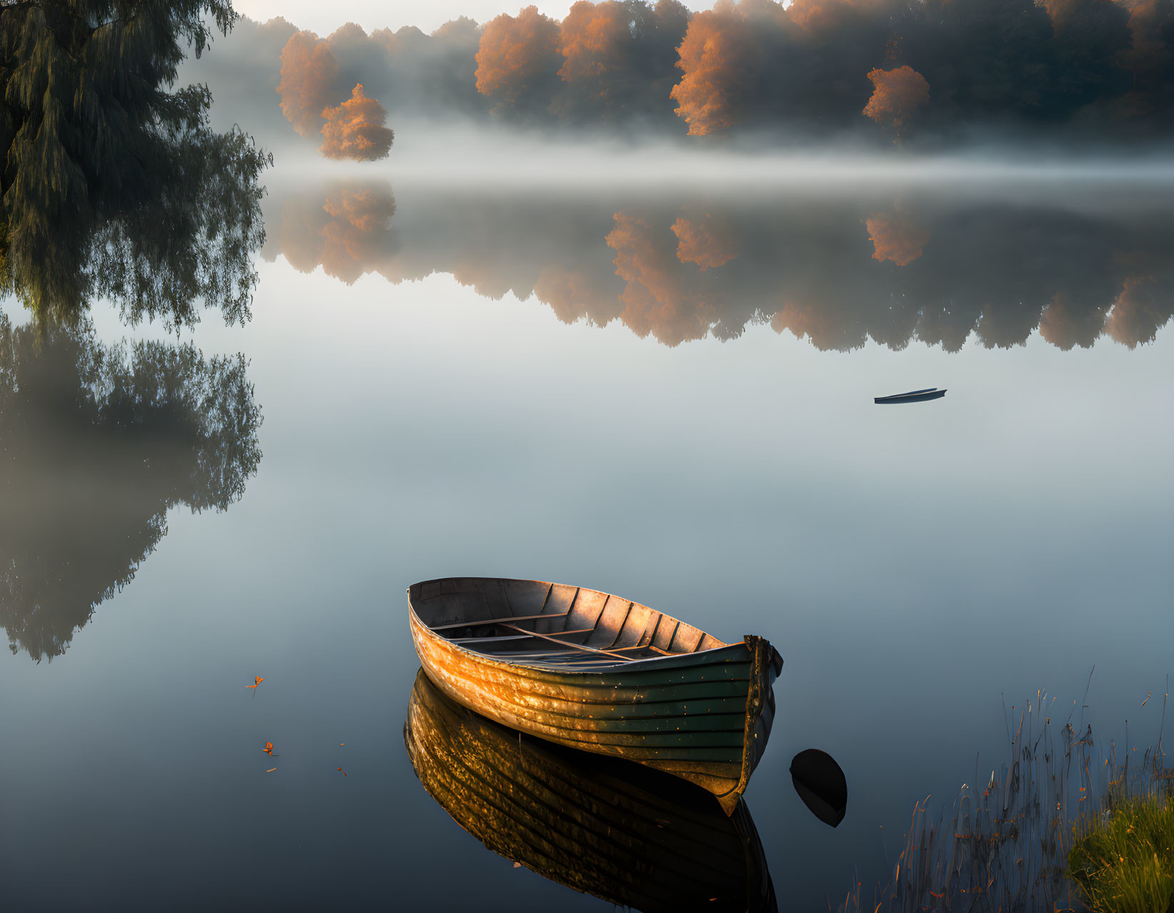 Tranquil landscape: boat on calm water with mist, trees reflecting at sunrise or sunset