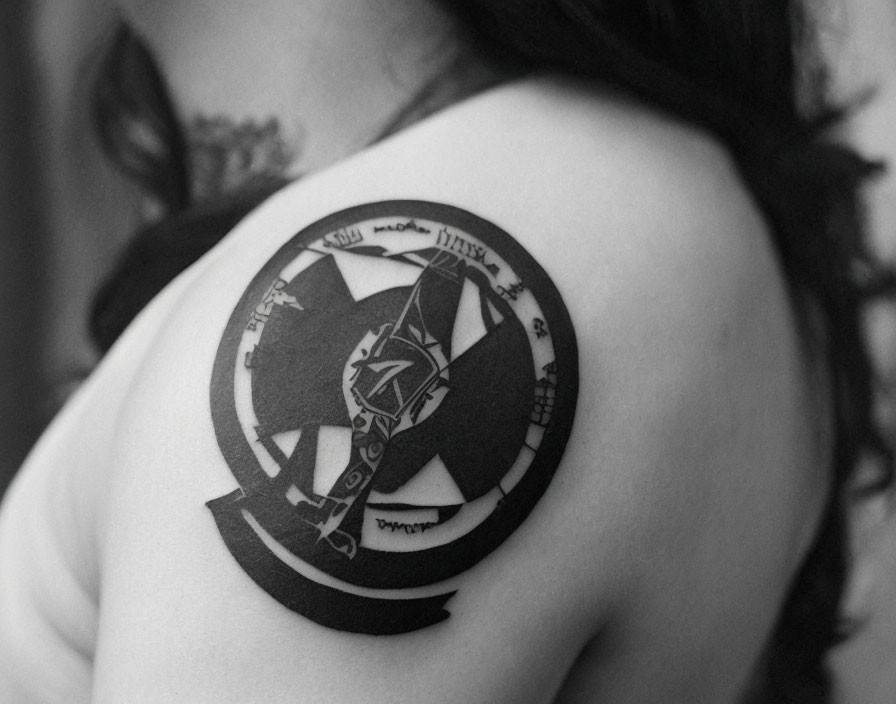 Detailed circular tattoo with symbols and text on shoulder