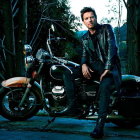 Man in leather jacket on classic motorcycle in forest with dramatic lighting