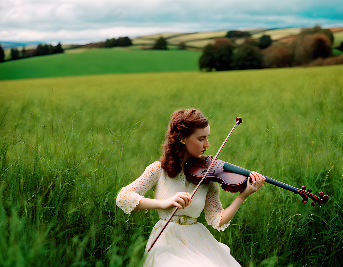 Woman in white dress playing violin in lush green field under cloudy sky