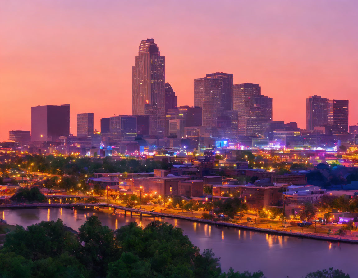 City skyline at dusk with illuminated buildings against pink and purple sky reflected in river.