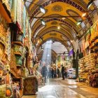 Vibrant marketplace with fruit stalls, spices, and cloaked figures in arched alley