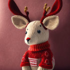 Knitted deer figurine with red antlers and floral chest on pink background