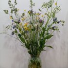 Decorative bouquet with gold and purple foliage in a green vase on gray background