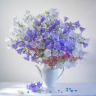 Blue Flowers and Greenery Bouquet in Clear Glass Vase on Soft Purple Background