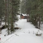 Red cabin and smaller structure in snowy forest under overcast sky