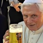 Elderly man in white suit and hat with beer glass, people in background