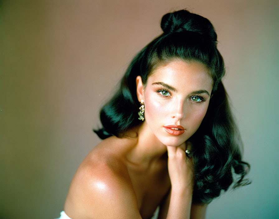 Dark-haired woman in updo with makeup and earrings against soft background