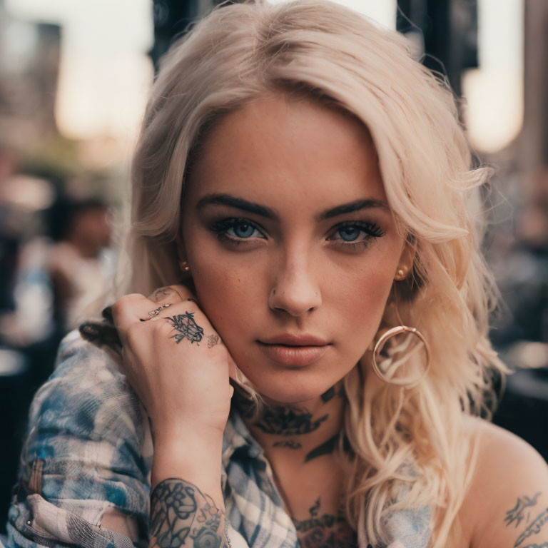 Blonde woman with tattoos and hoop earrings in a thoughtful pose