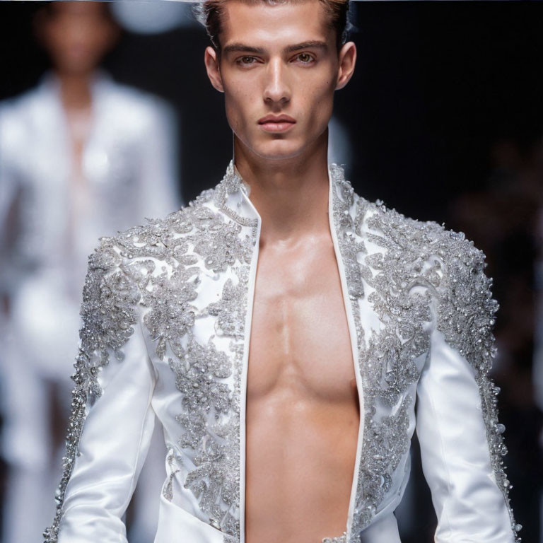 Male model showcases white ornately embellished jacket on runway