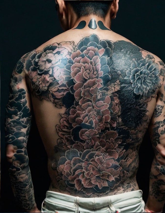 Elaborate floral back tattoos on person against black background