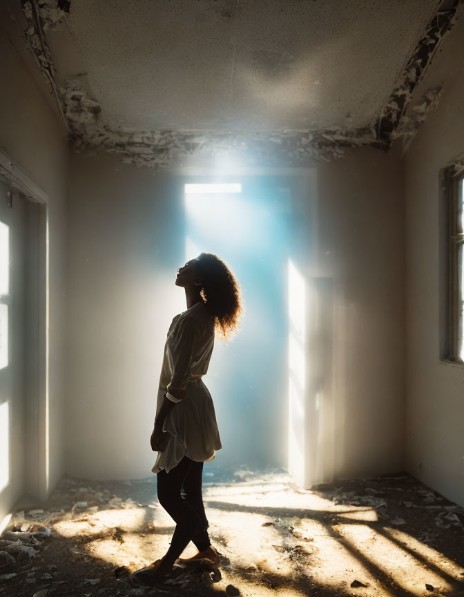 Silhouetted figure in abandoned room with light beam and debris