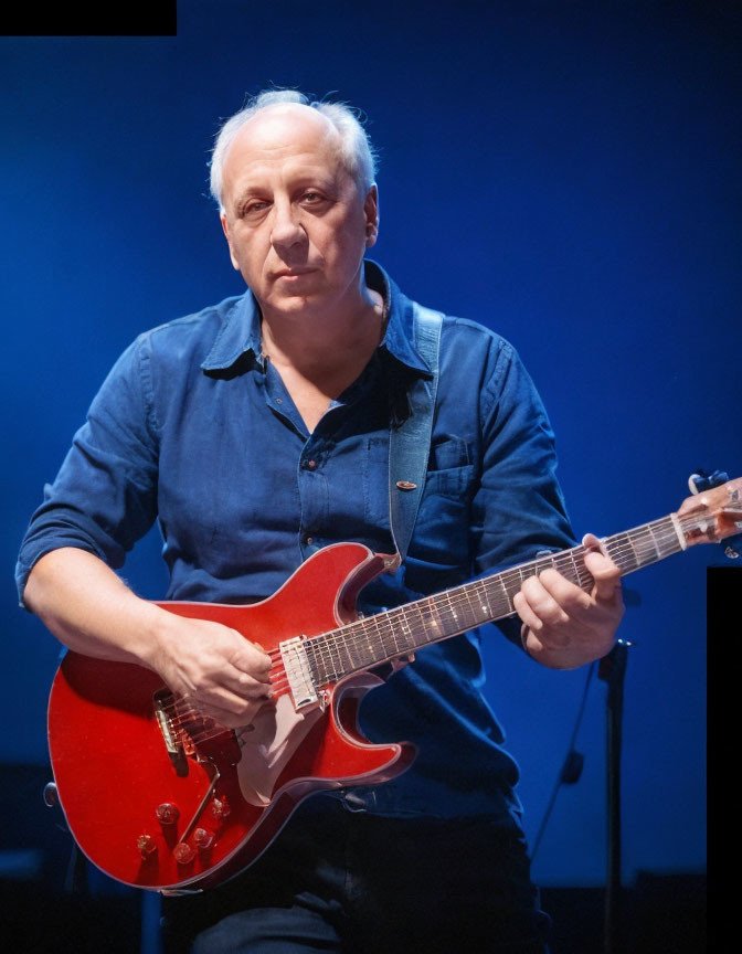 Man Playing Red Electric Guitar on Stage in Dark Blue Shirt