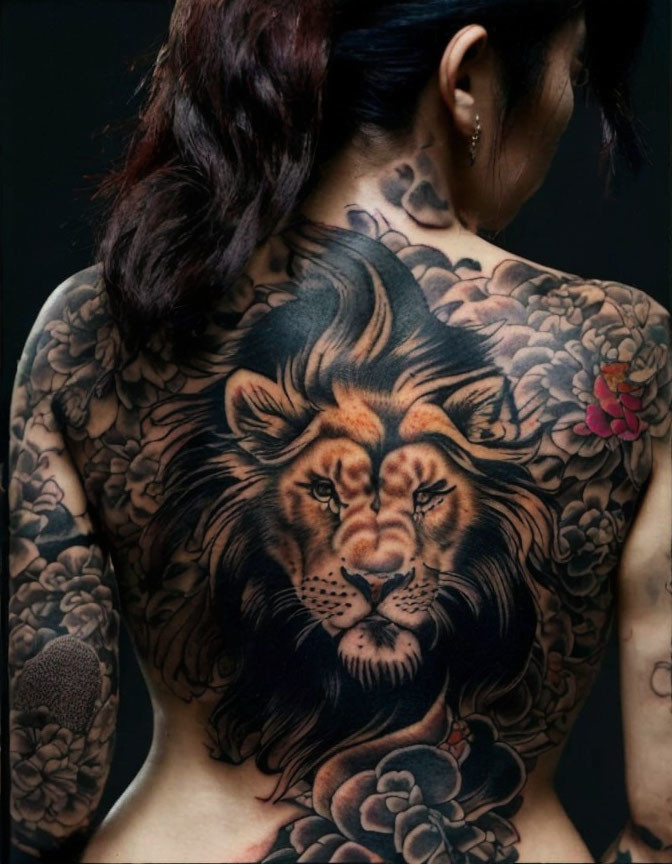 Detailed lion head tattoo surrounded by floral designs on person's back