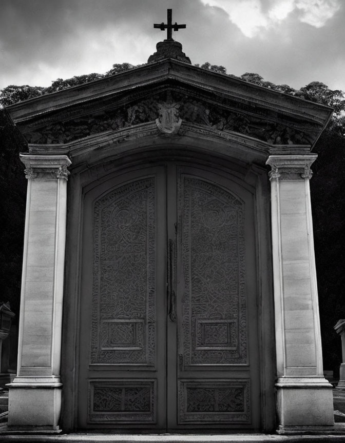 Ornate mausoleum entrance with cross, pillars, and cloudy sky