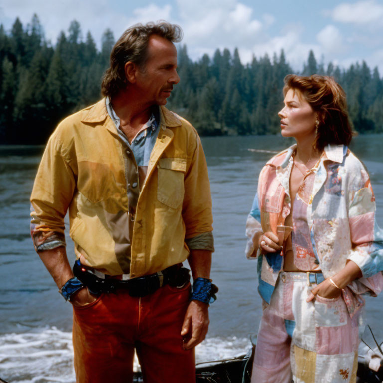 Man and woman in colorful attire standing by riverbank gaze into distance