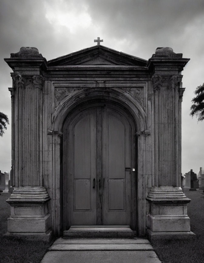 Monochrome image: Ornate mausoleum entrance with stone columns and wooden door