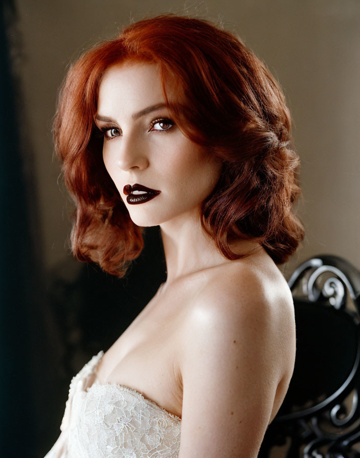 Red-haired woman in black lipstick and white lace dress poses elegantly.