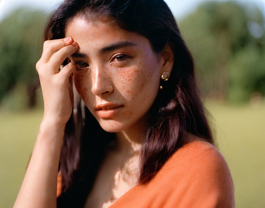 Freckled young woman in rust-colored top against green backdrop