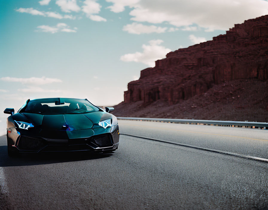 Black sports car on empty highway with rocky hills and clear blue sky