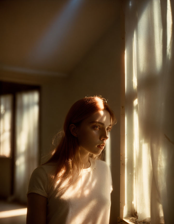 Woman gazing outside in warm light through sheer curtain