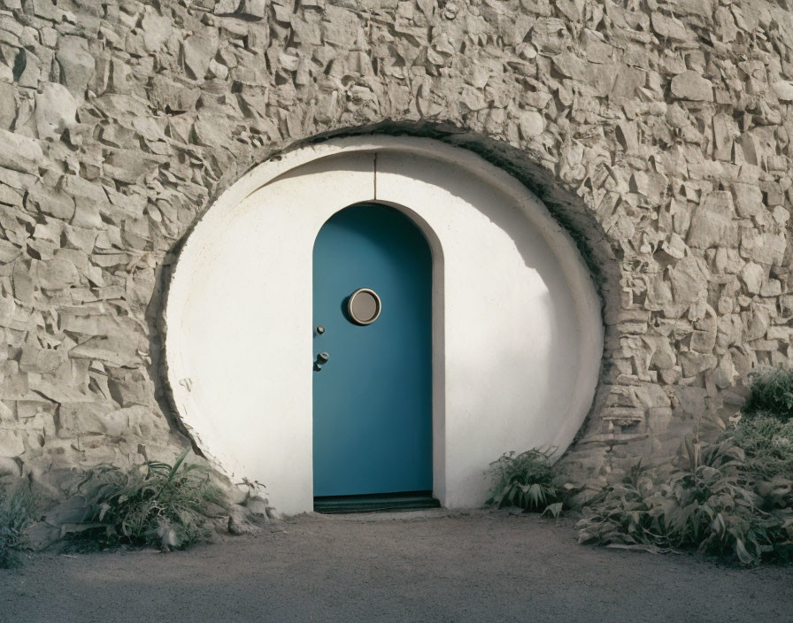 Blue Door with Circular Window in White Arch on Stone Wall with Plants