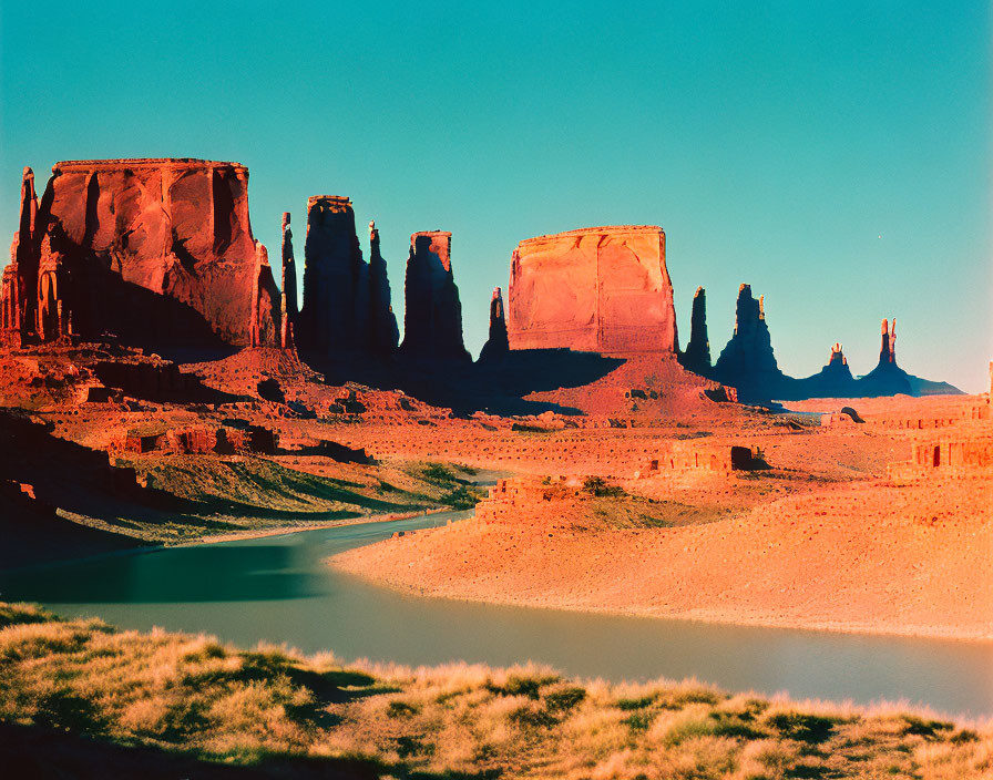 Majestic red rock formations above serene desert river in clear blue sky