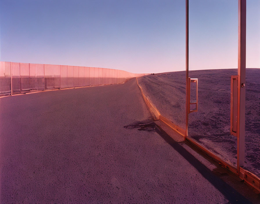 Curved metal fence on deserted road with two open gates under mauve sky