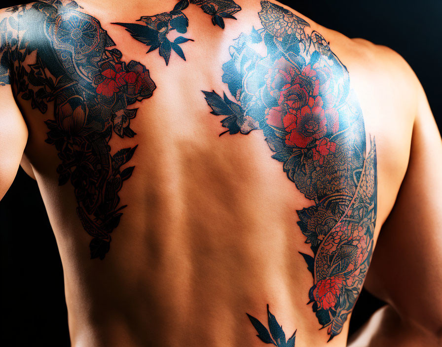 Detailed floral tattoo on person's back with vibrant red flowers and dark leaves.