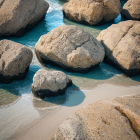 Turquoise water flowing around boulders on sandy beach