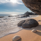 Scenic beach with smooth pebbles, waves, and rocky cliffs under sunlit sky