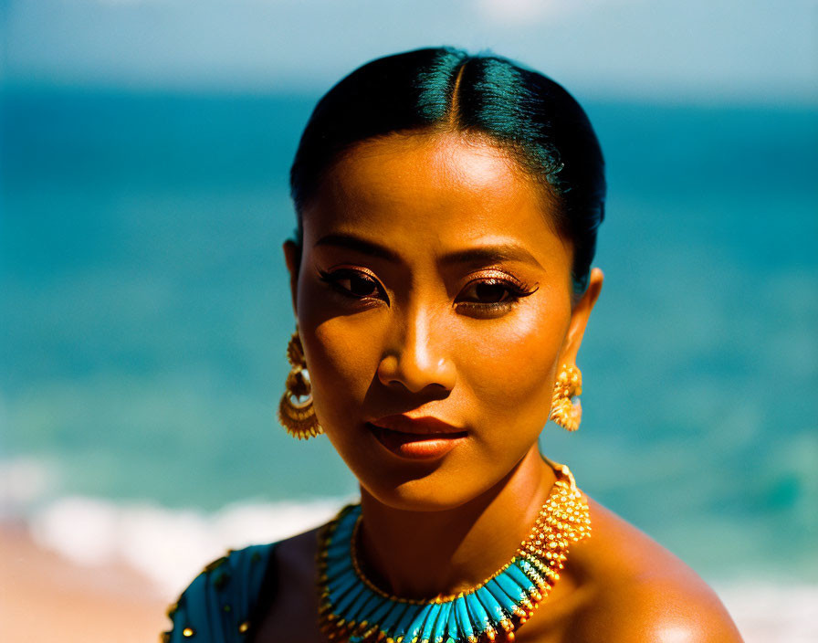 Woman with Tanned Skin and Dark Hair in Golden Jewelry on Beach Background