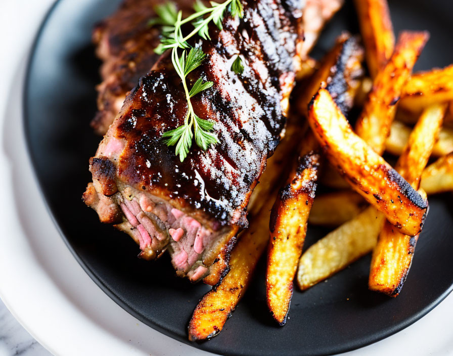 Grilled rack of ribs with char marks and seasoned fries on black plate