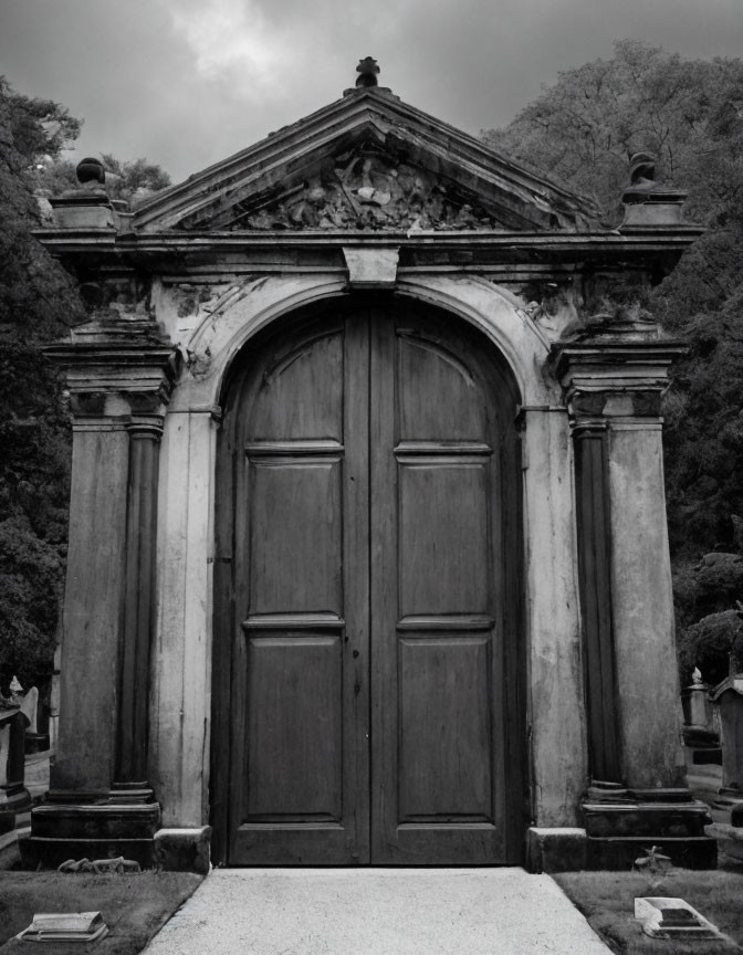 Weathered wooden door in ornate stone archway with grave markers under overcast skies