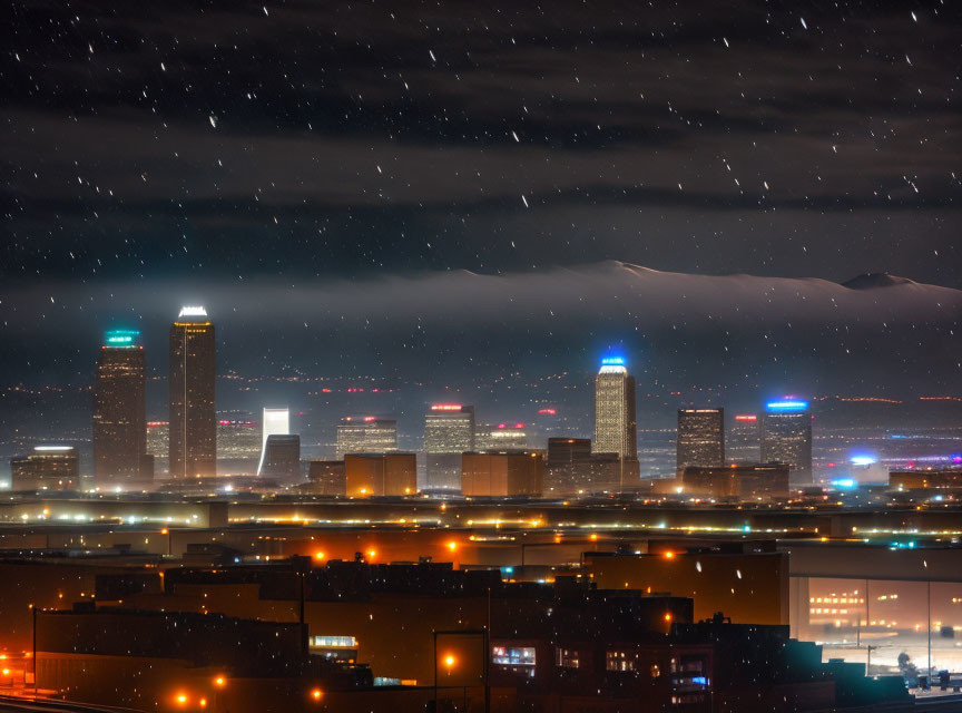 Snowy night city skyline with illuminated buildings and distant mountains.