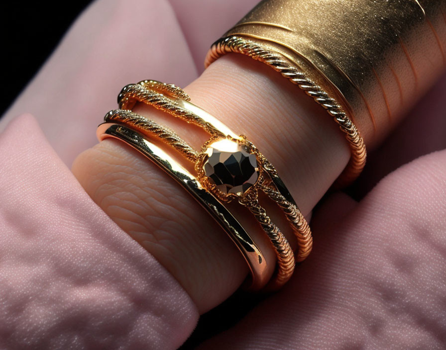 Hand with Gold Bracelets and Black Gemstone Ring on Pink Surface