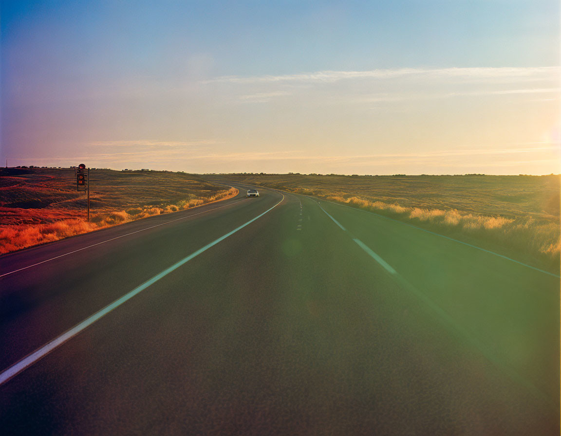 Desolate road under soft sunset with traffic signs and grassland