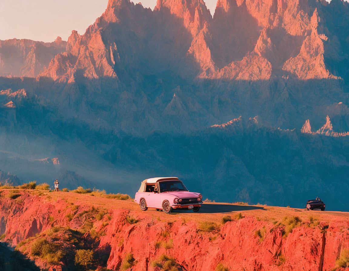 Vintage Car on Mountain Road at Sunset with Sharp Peaks and Person Standing Nearby