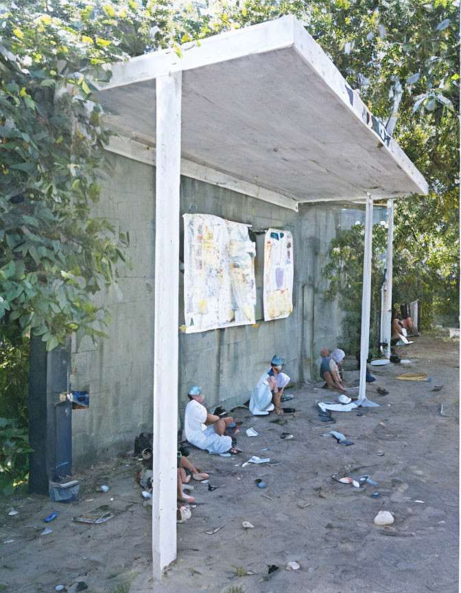 Group of People Sitting Under Shelter with Posters Surrounded by Trees