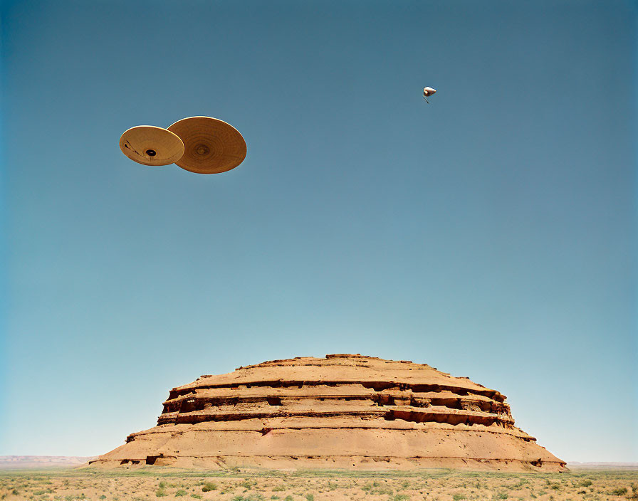 Wooden spools floating above desert mound under clear blue sky