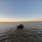 Boat on Calm Waters at Sunrise with Distant Cliffs