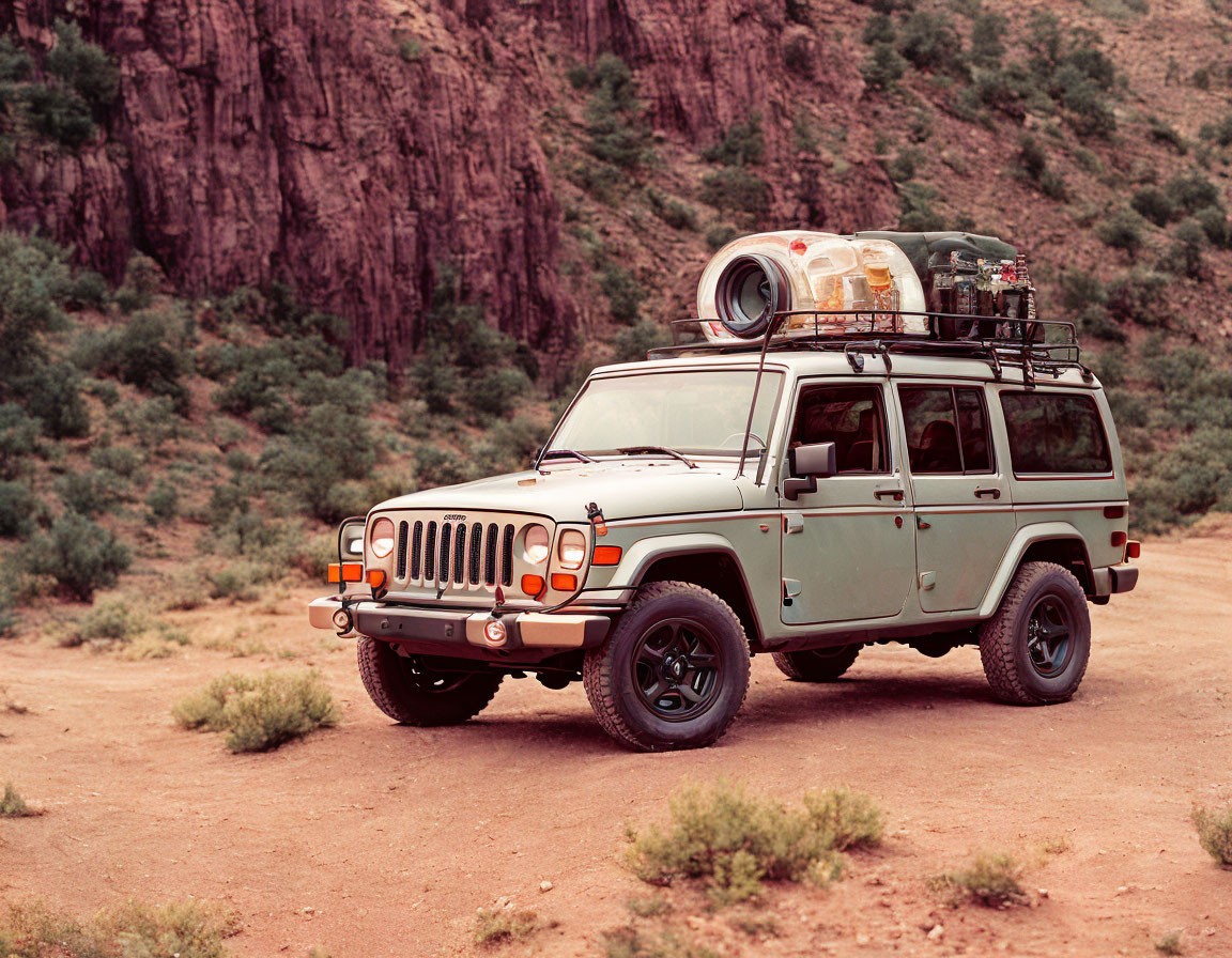 Green Off-Road Vehicle with Roof Rack and Spare Tires on Dirt Path by Reddish Cliffs