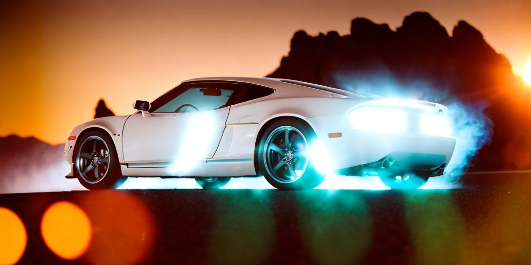 White Sports Car with Illuminated Wheels Emitting Smoke Against Orange Sky and Mountain Silhouette