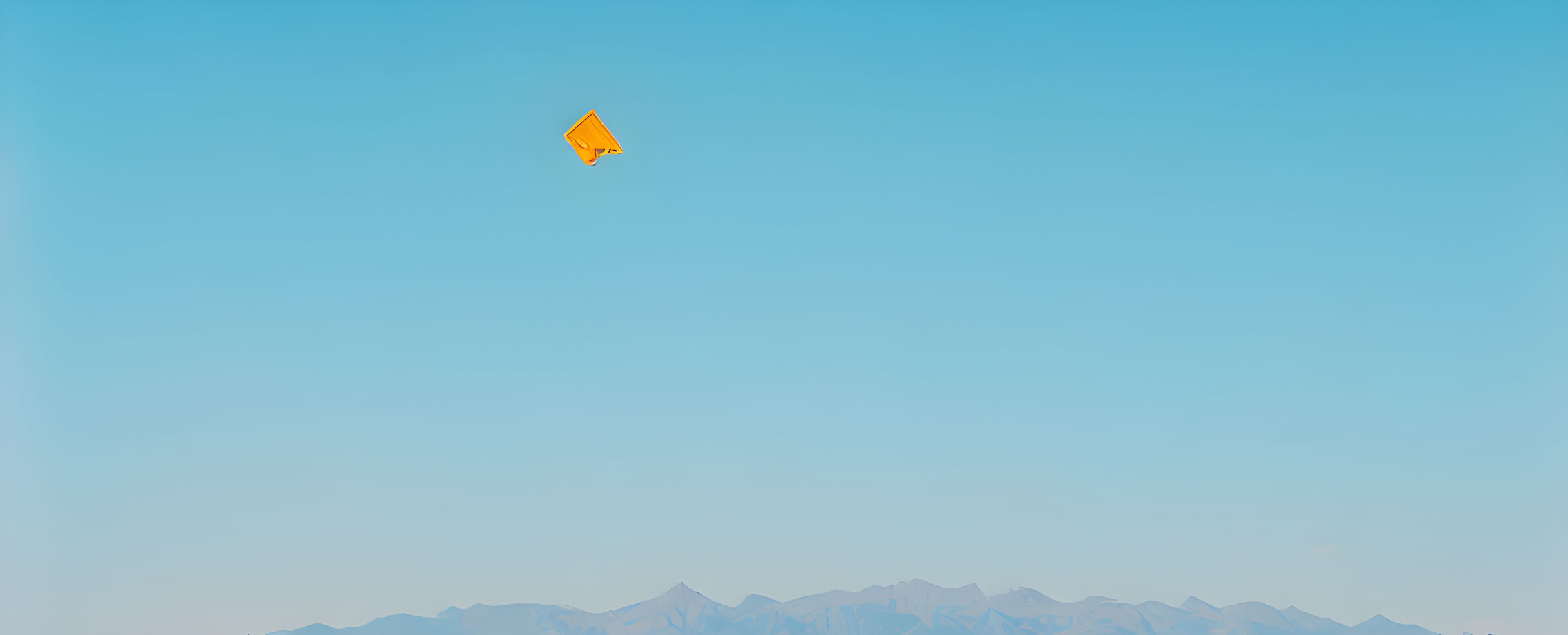 Orange kite flying high over mountain ranges in clear blue sky