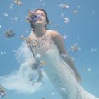 Illustration of woman with floral adornments in water with swimming fishes & white bird