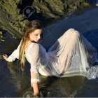 Traditional woman in ornate headdress by serene waterfall with blue fish.